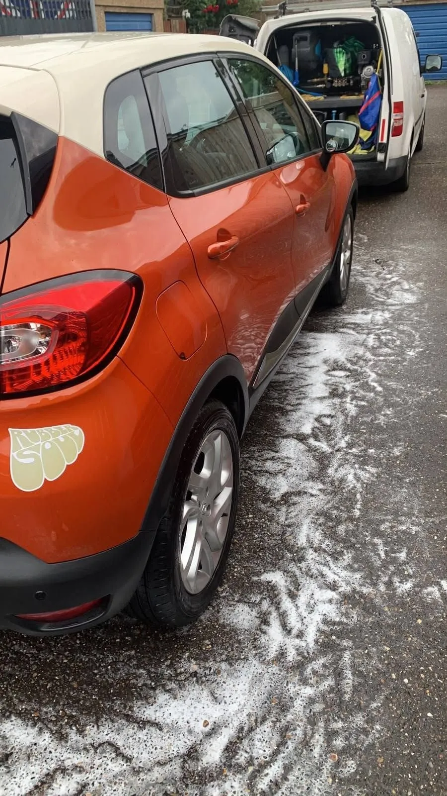 Orange Renault Captur on a street after a snow foam wash, foam still on the road beside the car