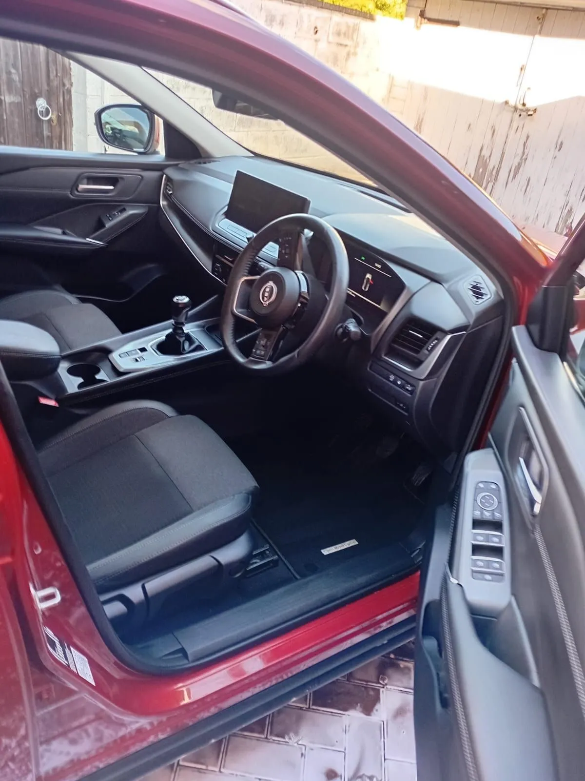 Front cabin of a red Nissan Qashqai after a valet: clean dark seats, dashboard and door trims, door open on a brick driveway