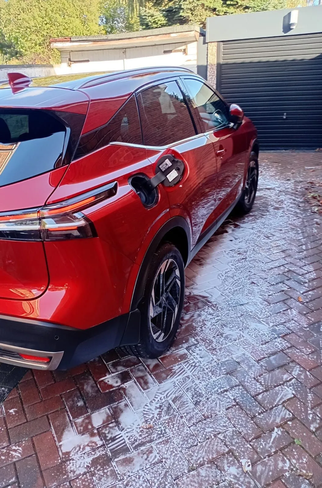 Rear three-quarter view of a red Nissan Qashqai on a block-paved driveway, foam drying on the paving after the wash