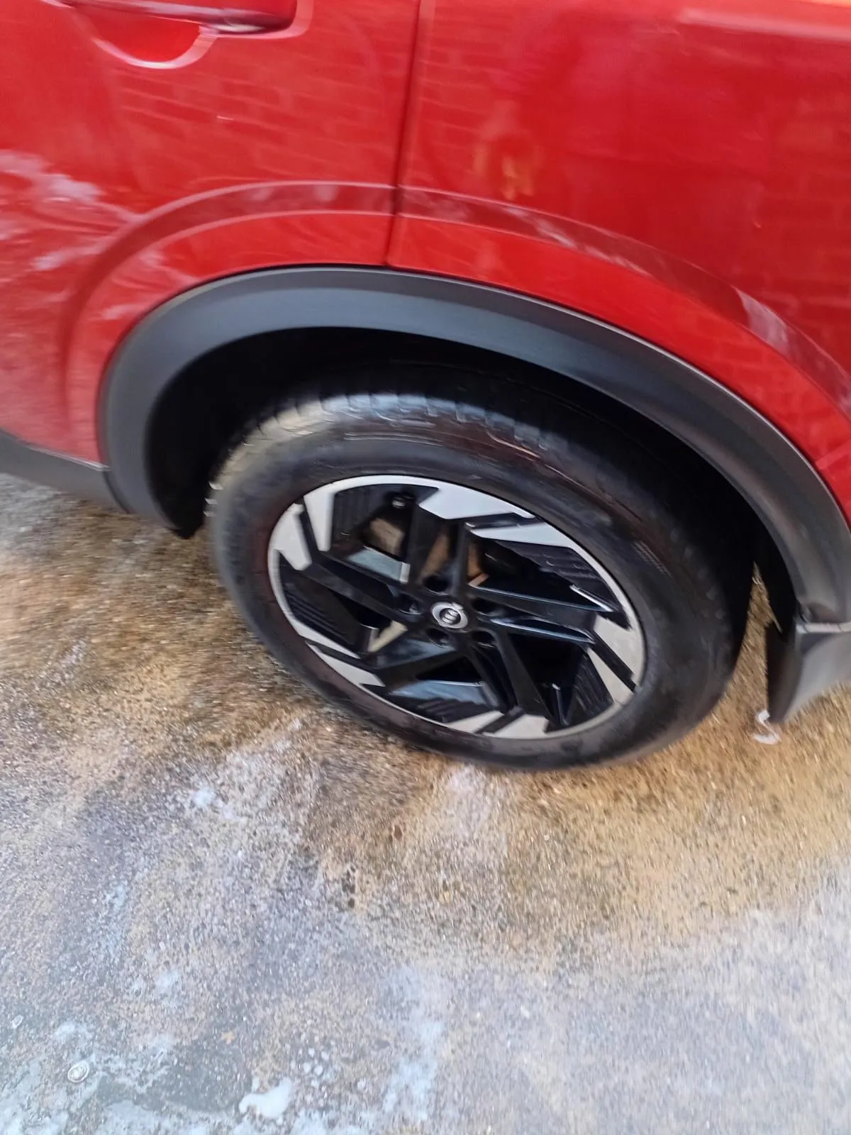 Black alloy wheel of a red Nissan Qashqai, cleaned and dressed, with wash foam on the ground