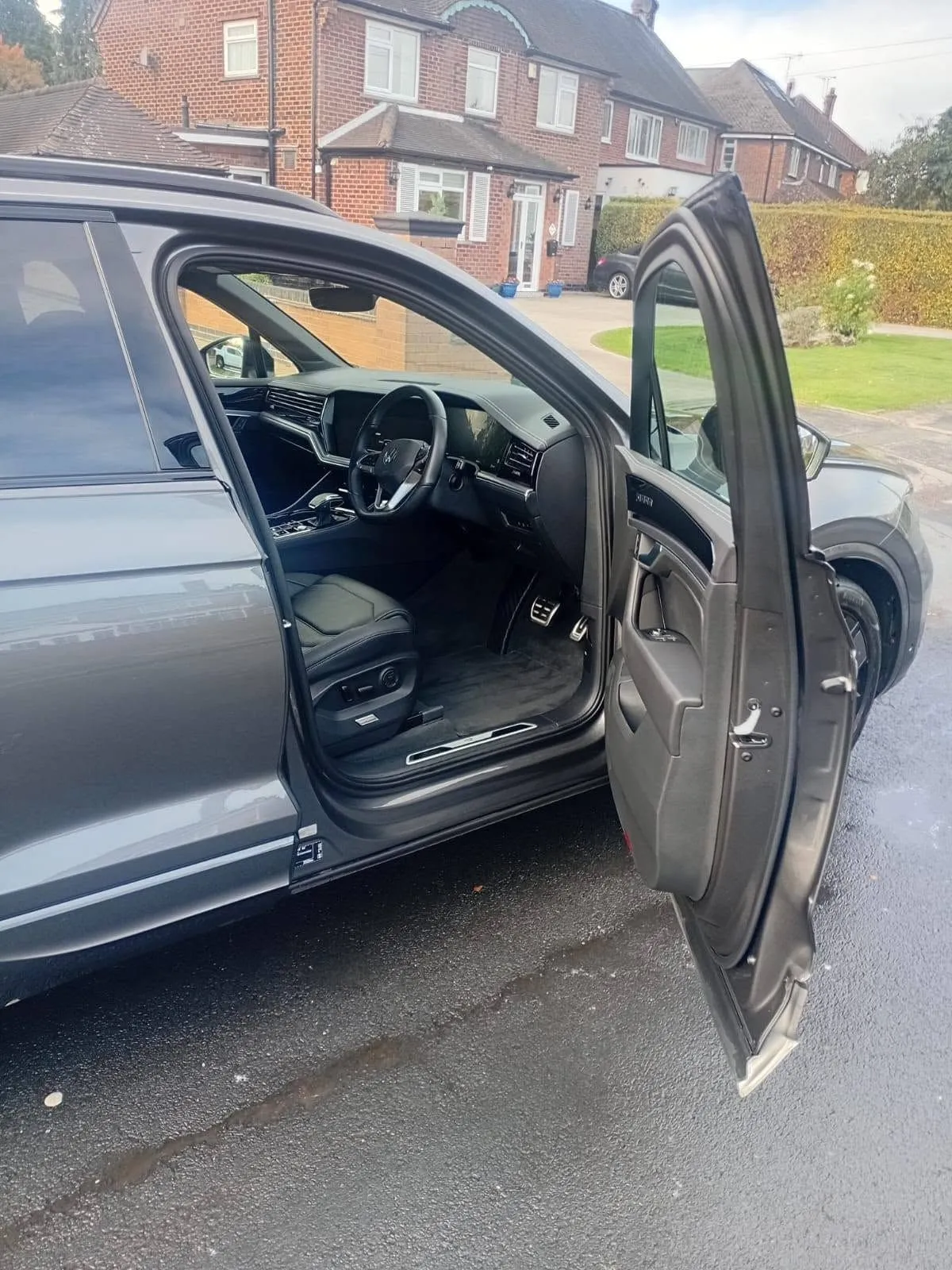Driver's door open on a grey Volkswagen Touareg after a valet, clean cabin and sills, parked on a residential street